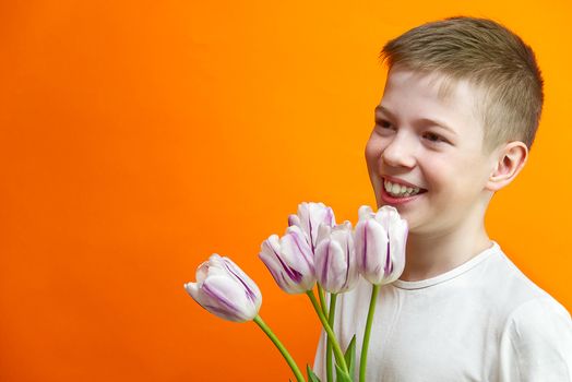 smiling young handsome boy on an orange background with tulips in hands. Children happiness