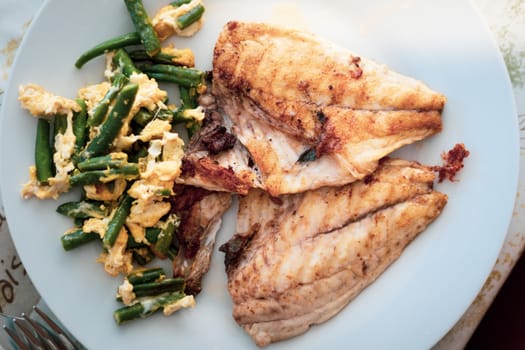 Grilled seabrem fish fillet and scrambled eggs and vegetables on plate, top view. This fish is widely used in Mediterranean cooking