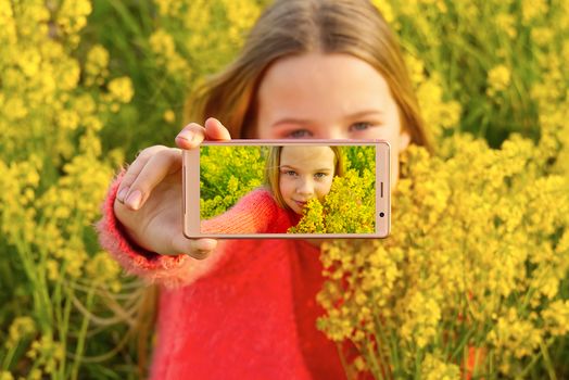 Happy smiling girl making self portrait on smartphone in meadow. young girl making selfie on smartphone laying in green grass with yellow flowers