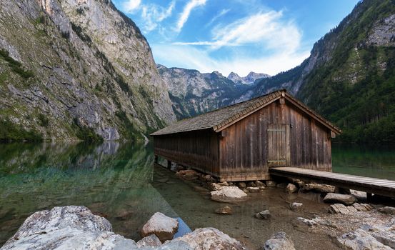 Panoramic view traditional old wooden boat house at scenic Lake Obersee on a beautiful day with foggy clouds in autumn, Bavaria, Germany