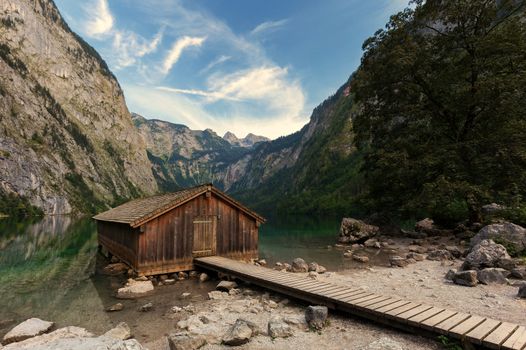 Panoramic view traditional old wooden boat house at scenic Lake Obersee on a beautiful day with foggy clouds in autumn, Bavaria, Germany