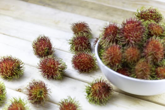 fresh rambutan in white blow and some drop on wood table. Soft focus and focus to rambutan on wood table