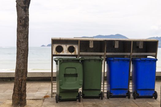 Green and blue bin for different collection Of Recycle Materials on  footpath near beach
