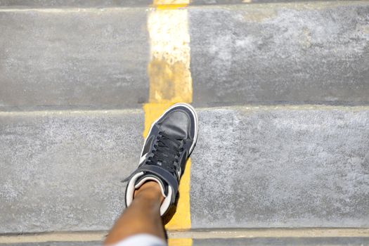 Man legs with long sneakers walking down public stair with yellow line in the city. 