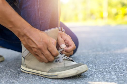 Man in blue jeans tying up sneakers on road