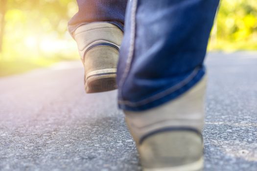 Man in jeans and sport sneakers walking on road. Focus on sneakers. With copy space for text or desing