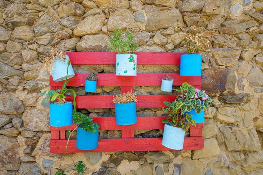 Red wooden pallet attached to an old wall with recycled flowerpots