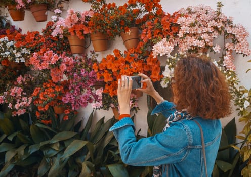 Tourist woman taking photos of a typical spanish white walls street, full of flowerpots on the floor and on the walls, in the rural town of Hervas, Extremadura, Spain.