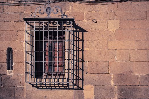 Window with bars on a stone facade in Casa del Doctor Trujillo, and old medieval palace in Plasencia, Esxtremadura, Spain.