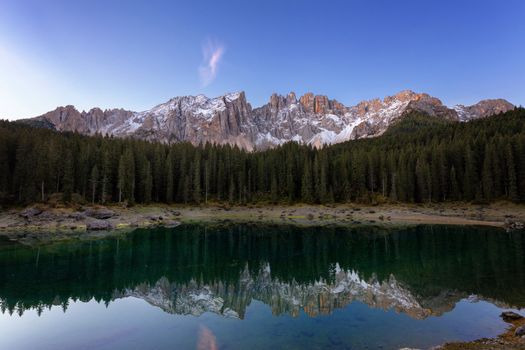 Beautiful sunrise at Carezza lake with light hitting the peaks, Dolomites, Italy