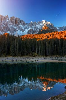 Beautiful sunrise at Carezza lake with light hitting the peaks, Dolomites, Italy