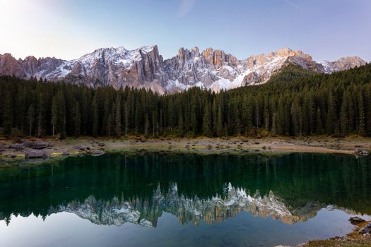 Beautiful sunrise at Carezza lake with light hitting the peaks, Dolomites, Italy