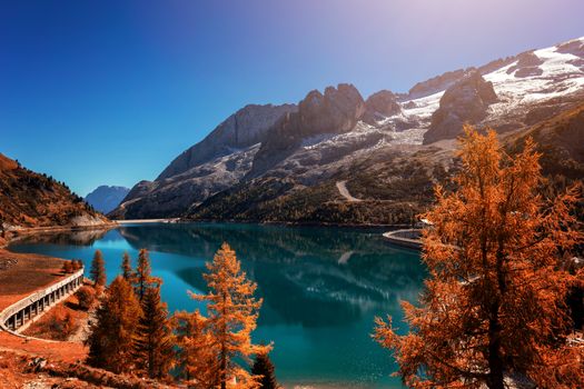 Beautiful autum colors at Fedaia lake with Marmolada peaks covered by ice, Dolomites, Italy