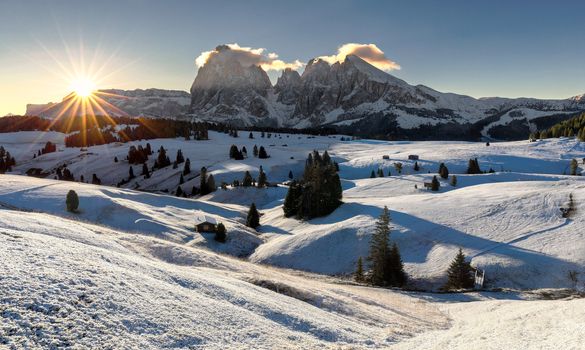 Beautiful view of traditional wooden mountain chalets on scenic Alpe di Siusi with famous Langkofel mountain peaks in the background in golden morning light at sunrise, Dolomites, South Tyrol, Italy