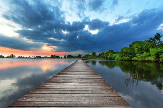 Wooden path bridge over lake at stormy sunset