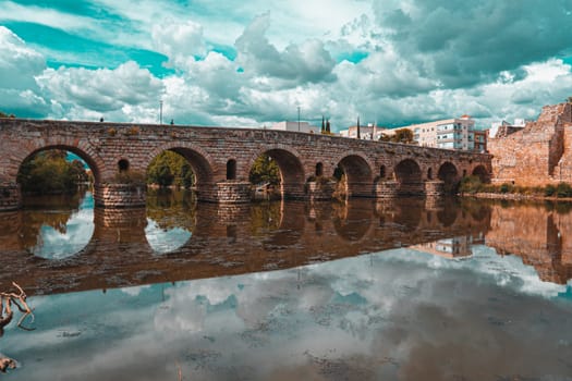 Orange and teal view of the Roman bridge of Merida with its reflection on the Guadiana river. Merida. Spain.The Archaeological Ensemble of Merida is declared a UNESCO World Heritage Site Ref 664