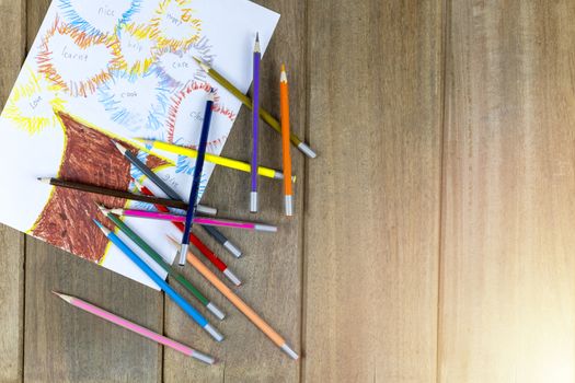 Many color pencils draw the picture on white paper on wood bakcground. With copy space for text or design.
