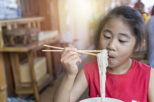 Asian child girl with red dress eating small noodles soup with chopsticks