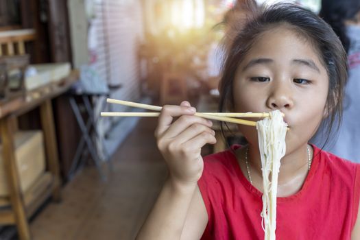 Asian child girl with red dress eating small noodles soup with chopsticks at restaurant