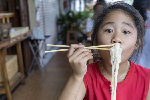 Asian child girl with red dress eating small noodles soup with chopsticks