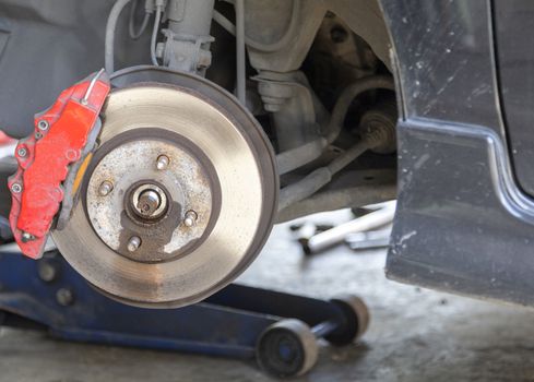 Front disc brake on black color car with red cover brake caliper process of new tire replacement