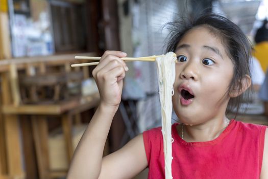 Asian child girl with red dress eating small noodles soup with chopsticks