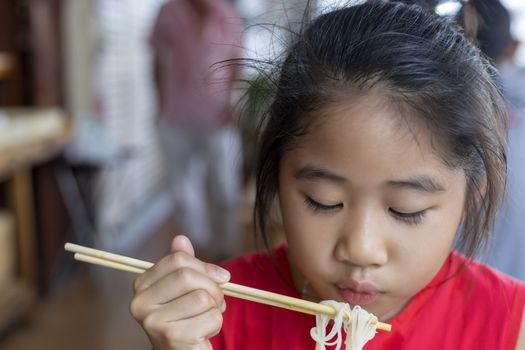 Asian child girl with red dress eating small noodles soup with chopsticks