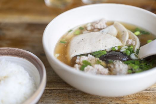 Soup with pock, pock stick, mushroom, vegetable in white bowl near have rice in small bowl on wood table. with copy space for text or design