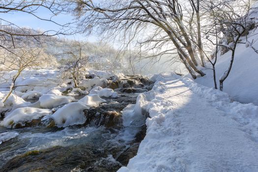 Winter path covered by snow and river flowing thru plitvice lake, Croatia