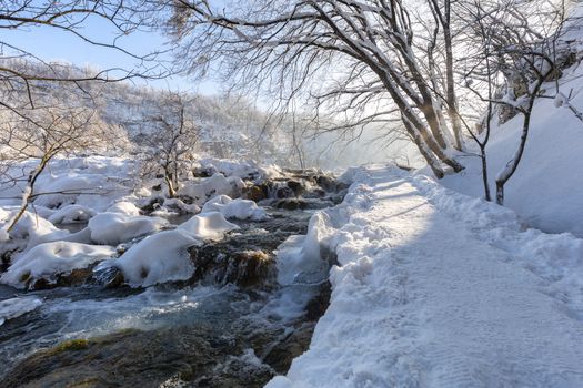 Winter path covered by snow and river flowing thru plitvice lake, Croatia