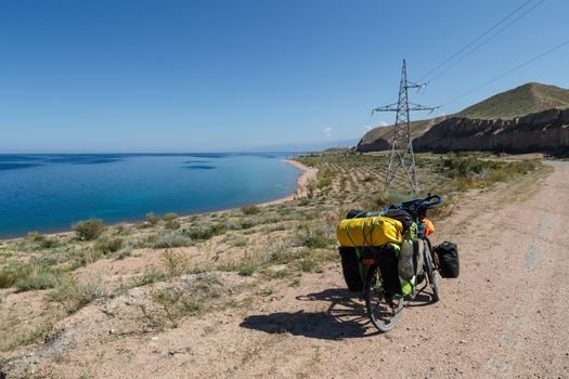 traveler's bike with bags stand on the road near Issyk-Kul Lake, landscape, Kyrgyzstan, tourist bike