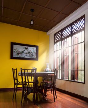 Wooden round table and chair chiness style near window have ray of light on wood floor and yellow wall have lotus chiness picture