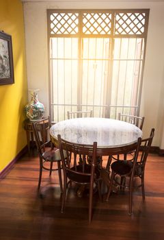 Wooden round table and chair chiness style near window have ray of light on wood floor and yellow wall have lotus chiness picture