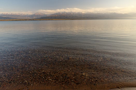 South shore of Issyk-kul lake in Kyrgyzstan, clear water in the lake and mountains with snowy peaks in the background