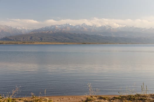 South shore of Issyk-kul lake in Kyrgyzstan, clear water in the lake and mountains with snowy peaks in the background