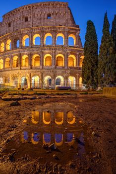 The illuminated Colosseum in Rome at twilight with a reflection in a puddle