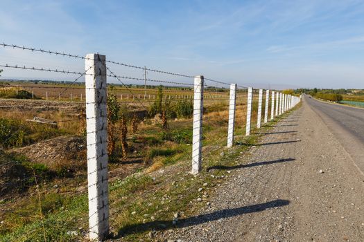 barbed wire fence along the road, state border between Kyrgyzstan and Uzbekistan