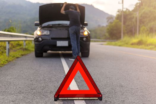Red triangle sign on road for warning have car with breakdown open car hood and man fixing a car. 