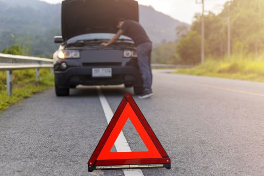 Red triangle sign on road for warning have car with breakdown open car hood and man fixing a car. 
