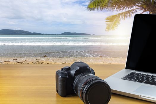Digital camera and laptop on wood table with sea and sky background. With copy space for text or design.