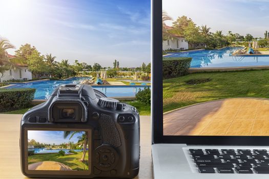 Picture of laptop computer and back screen digital camera on wood table with garden and pool background.