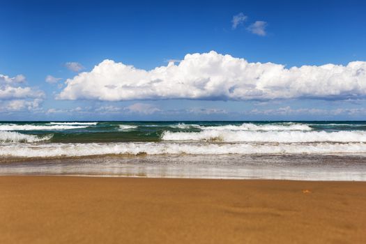 Sunny day on the beach with big waves and white clouds