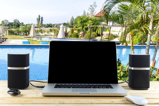 Work desk laptop mouse and speakers on wood table with garden and swimming pool background. With copy space for text or design
