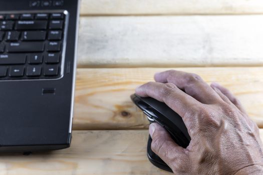 Hand hold mouse control laptop on wood table. With copy space for text or design.