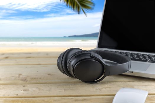 Headphones and laptop on wood table with beach background. With copy space for text or design. Technology concept.