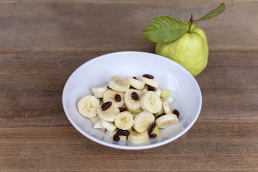 healthy food banana slide guava block and raisins in white bowl on wood table. With copy space for text or design.