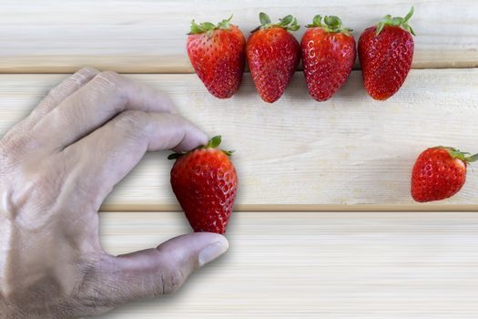 Hand man holding fresh strawberrie with fresh strawberries on wood table background with copy space for text or design.