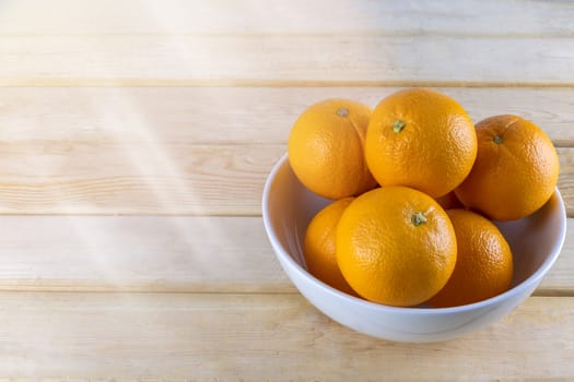 Fresh oranges in white bowl on wood table.