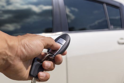 Hand man hold button unlock on the car remote control for unlock door white car.