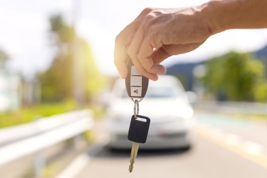 Hand man holding car keys and blur car in background.